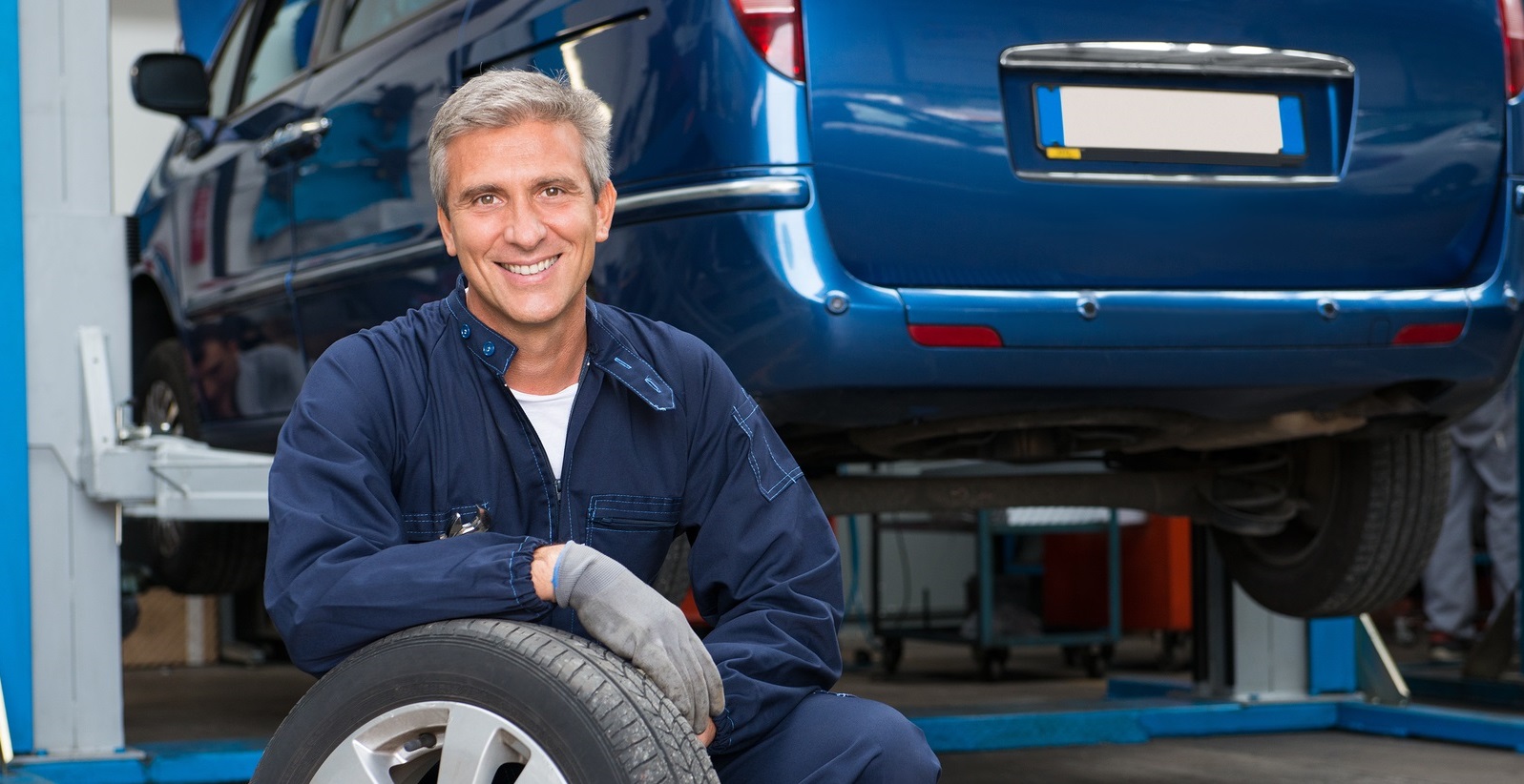 auto technician leaning against a tire, van on lift